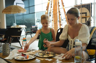 Young mother and her daughter paint Halloween cookies in a spacious modern workshop clipart