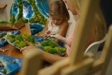 Genç bir anne ve kızı birlikte canlı doğal manzaralar yaratıyor. 