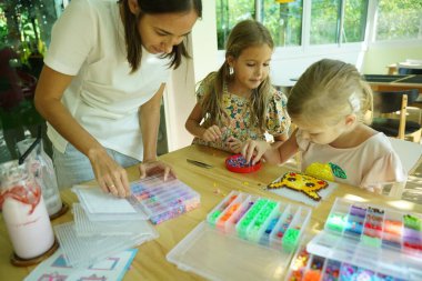 Sanat öğretmeni atölyede iki kıza termo mozaik montajı öğretiyor. 