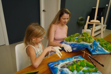 Genç bir anne ve kızı birlikte canlı doğal manzaralar yaratıyor. 