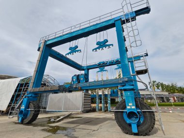 Bulutlu bir gökyüzünün altında endüstriyel bir servis alanına yerleştirilmiş tekneler için büyük mavi bir vinç.