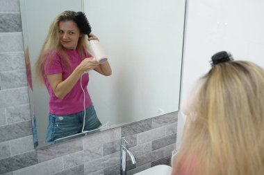 Bir kadın uzun saçlarını kuruturken aynı zamanda onu tarıyor.