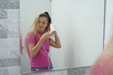 Bir kadın uzun saçlarını kuruturken aynı zamanda onu tarıyor.