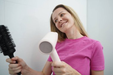 Bir kadın uzun saçlarını kuruturken aynı zamanda onu tarıyor.