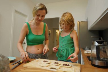 Bir anne ve kızı sıcacık bir mutfakta mutlu bir şekilde yemek pişiriyor.