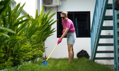 Evinin arka bahçesindeki çimenleri tırmıklayan genç bir kadın. 