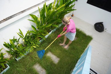 Evinin arka bahçesindeki çimenleri tırmıklayan genç bir kadın. 