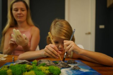 Genç bir anne ve kızı birlikte canlı doğal manzaralar yaratıyor. 