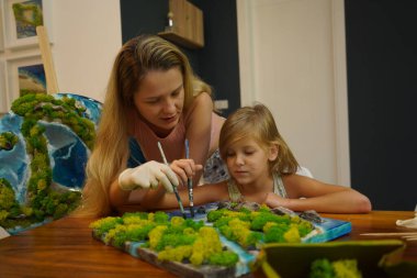 Genç bir anne ve kızı birlikte canlı doğal manzaralar yaratıyor. 