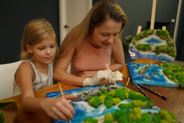 Genç bir anne ve kızı birlikte canlı doğal manzaralar yaratıyor. 