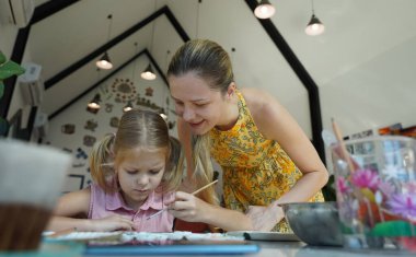 Genç bir anne ve kızı evde sanatsal bir seansın keyfini çıkarıyorlar. Renkli sanatlarıyla meşgul ve bağ kuruyorlar.