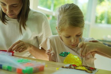 Sanat öğretmeni atölyede iki kıza termo mozaik montajı öğretiyor. 