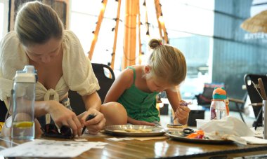 Genç anne ve kızı cadılar bayramı kurabiyelerini geniş bir modern atölyede boyuyorlar.