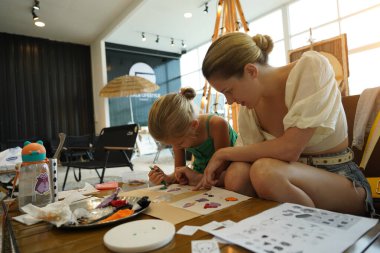 Genç anne ve kızı cadılar bayramı kurabiyelerini geniş bir modern atölyede boyuyorlar.