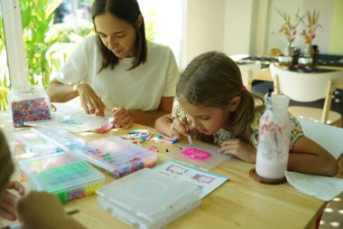 Sanat öğretmeni atölyede iki kıza termo mozaik montajı öğretiyor. 