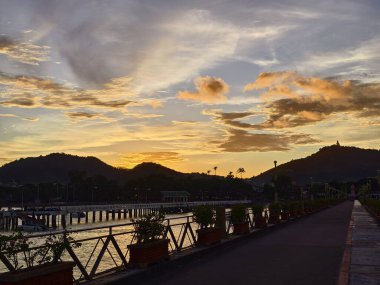 Nefis, sakin bir gün batımı manzarası. Dalgalı gökyüzüne karşı zarifçe siluetlenmiş balıkçı tekneleri.