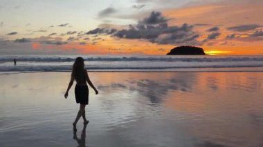 Gün batımında sakin sahil sahnesinde koşan ve yürüyen bir kadın. 