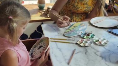 Genç bir anne ve kızı evde sanatsal bir seansın keyfini çıkarıyorlar. Renkli sanatlarıyla meşgul ve bağ kuruyorlar.