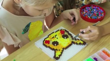 Sanat öğretmeni atölyede iki kıza termo mozaik montajı öğretiyor. 