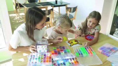 Sanat öğretmeni atölyede iki kıza termo mozaik montajı öğretiyor. 