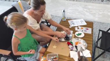 Genç anne ve kızı cadılar bayramı kurabiyelerini geniş bir modern atölyede boyuyorlar.