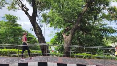 Bir kadın, yemyeşil ve çarpıcı kıyı manzaralarıyla çevrili güzel, dolambaçlı bir yolda koşuyor.