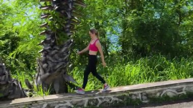 Bir kadın, yemyeşil ve çarpıcı kıyı manzaralarıyla çevrili güzel, dolambaçlı bir yolda koşuyor.