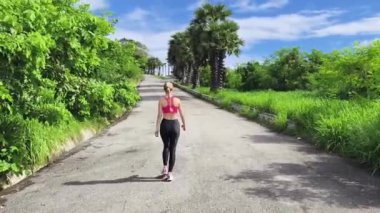 Bir kadın, yemyeşil ve çarpıcı kıyı manzaralarıyla çevrili güzel, dolambaçlı bir yolda koşuyor.