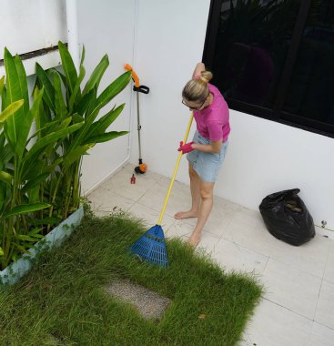 Evinin arka bahçesindeki çimenleri tırmıklayan genç bir kadın. 