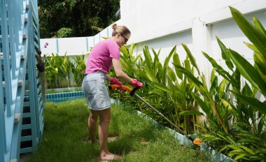 Genç bir kadın güzel bahçesini süslüyor canlı yeşilliğini ve açık hava aktivitelerine olan aşkını sergiliyor.