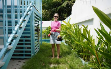 Genç bir kadın güzel bahçesini süslüyor canlı yeşilliğini ve açık hava aktivitelerine olan aşkını sergiliyor.