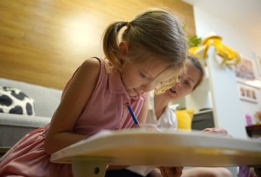 Genç bir anne ev ödevleriyle kızına destek olur.