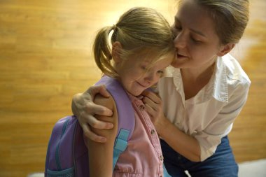 Genç anne, kızının okul için sırt çantasını toplamasına yardım ediyor.