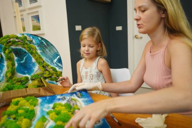 Genç bir anne ve kızı birlikte canlı doğal manzaralar yaratıyor. 