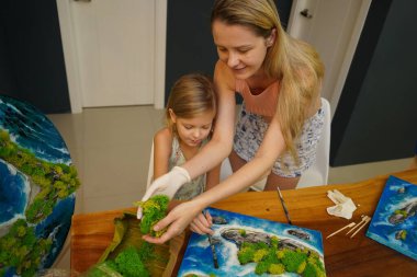 Genç bir anne ve kızı birlikte canlı doğal manzaralar yaratıyor. 