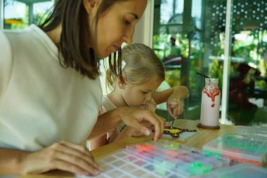 Sanat öğretmeni atölyede iki kıza termo mozaik montajı öğretiyor. 