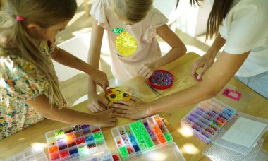 Sanat öğretmeni atölyede iki kıza termo mozaik montajı öğretiyor. 