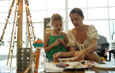Genç anne ve kızı cadılar bayramı kurabiyelerini geniş bir modern atölyede boyuyorlar.