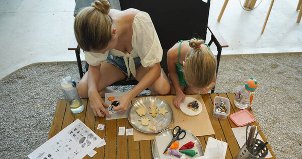 Молодая мать и ее дочь рисуют печенье на Хэллоуин в просторной современной мастерской