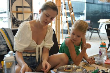 Genç anne ve kızı cadılar bayramı kurabiyelerini geniş bir modern atölyede boyuyorlar.