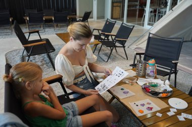 Genç anne ve kızı cadılar bayramı kurabiyelerini geniş bir modern atölyede boyuyorlar.