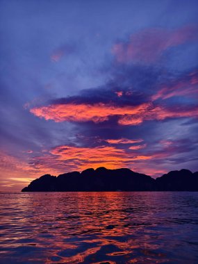 Çarpıcı bir günbatımı, kıyı şeridi manzarası boyunca sakin bir okyanusun üzerinde canlı renkler bırakıyor.