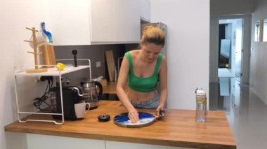 Genç bir kadın modern bir mutfakta kahve hazırlıyor ve içiyor..