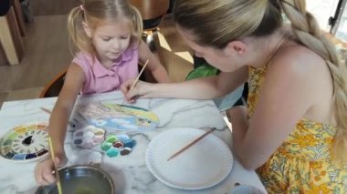 Genç bir anne ve kızı evde sanatsal bir seansın keyfini çıkarıyorlar. Renkli sanatlarıyla meşgul ve bağ kuruyorlar.