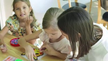 Sanat öğretmeni atölyede iki kıza termo mozaik montajı öğretiyor. 