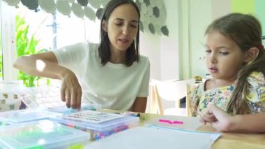 Sanat öğretmeni atölyede iki kıza termo mozaik montajı öğretiyor. 