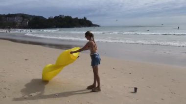 Kumsalda genç bir kadın, elinde bir içki ve akıllı telefonuyla sarı bir fasulye torbasının üzerinde uzanmış. 