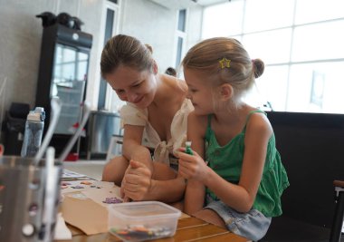 Young mother and her daughter paint Halloween cookies in a spacious modern workshop clipart