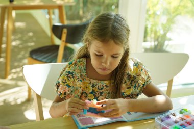 Sanat öğretmeni atölyede iki kıza termo mozaik montajı öğretiyor. 