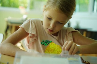 Sanat öğretmeni atölyede iki kıza termo mozaik montajı öğretiyor. 